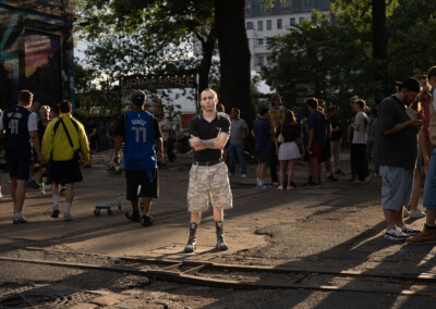 Die Aufnahme zeigt eine lebhafte Szene in Berlin, vermutlich im Stadtteil Kreuzberg. Der Fokus liegt auf einem einzelnen Mann, der sich im Vordergrund abseits der Hauptgruppe befindet. Die Atmosphäre wirkt urban und vielfältig.