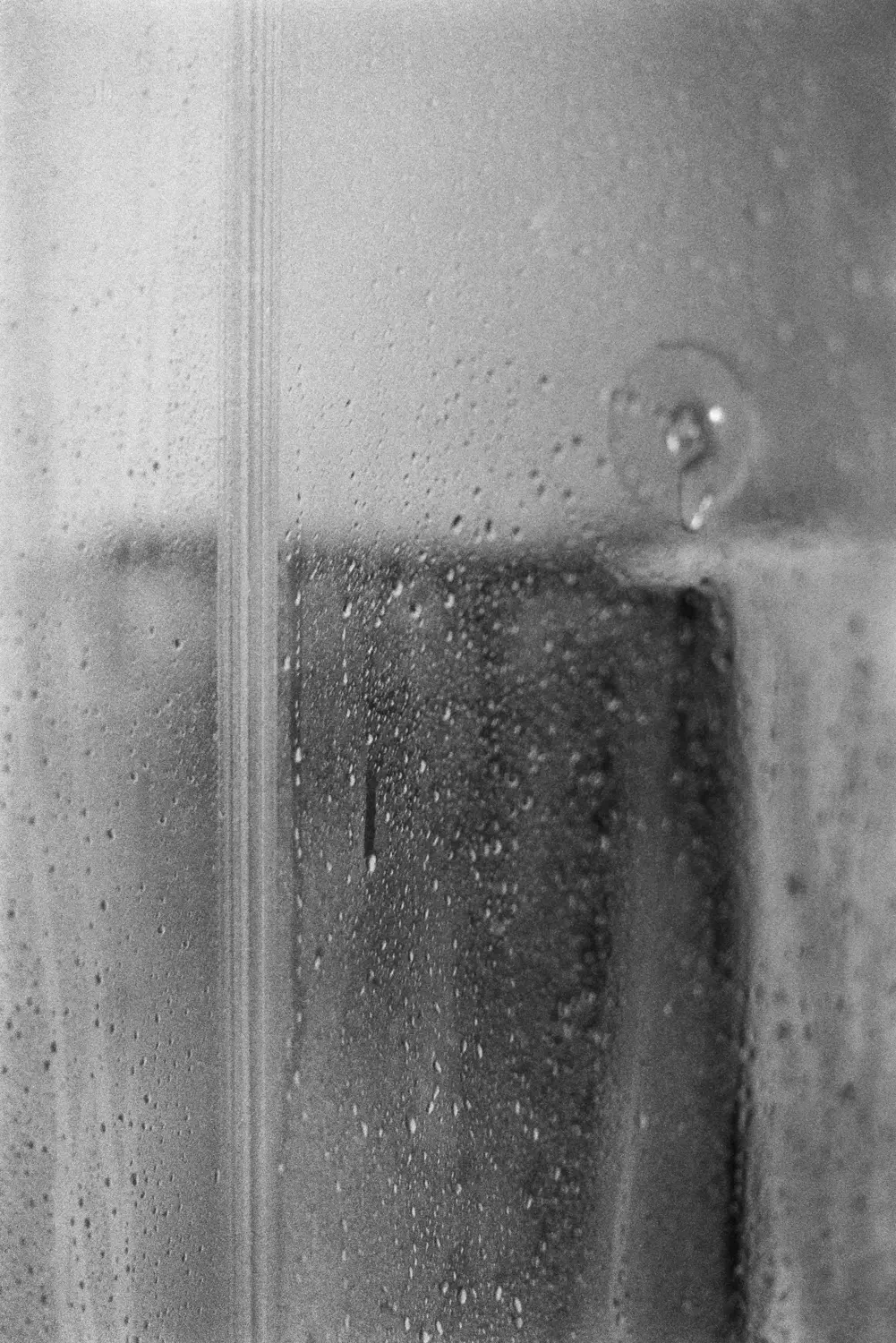 Die Aufnahme zeigt eine Szene aus Berlin, vermutlich in einem Innenraum aufgrund der Fenster und des Vorhangs. Der Regen erzeugt einen wirbelnden Effekt auf dem Glas, was die Atmosphäre verstärkt. Die Schwarzweißdarstellung betont die Textur und die Stimmung des Regens.