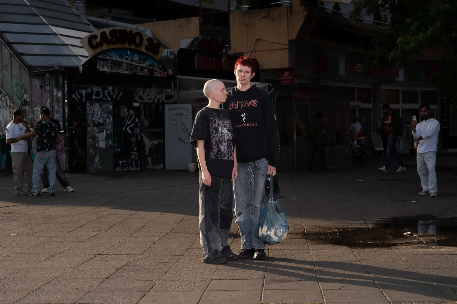 Die Aufnahme zeigt eine Gruppe von etwa sechs Studenten, vermutlich Mitglieder der Ostkreuzschule für Fotografie, vor dem Casino 36 in Berlin. Die Stimmung wirkt entspannt und beobachtend. Die Beleuchtung ist gedämpft, was einen urbanen Abendcharakter erzeugt.