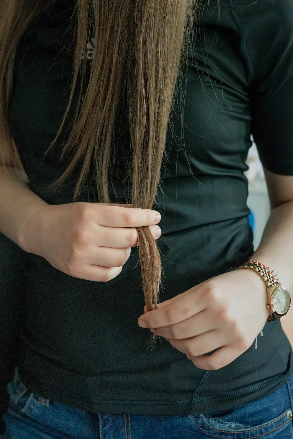 Die Aufnahme zeigt eine junge Frau, vermutlich ein Student der Ostkreuzschule für Fotografie, die Haarsträhnen in ihren Händen hält. Sie trägt einen schwarzen T-Shirt, Jeans und eine Armbanduhr mit roten Ziffern. Die Szene ist wahrscheinlich im Rahmen einer Gruppenausstellung 