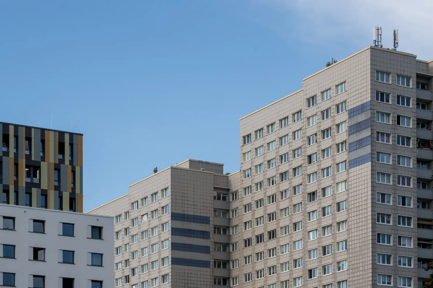 Das Bild zeigt eine Szene mit mehreren Wohnblöcken unter einem klaren Himmel. Es handelt sich um eine Stadtlandschaft, die wahrscheinlich in Berlin aufgenommen wurde, da es sich um eine Ausstellung der Ostkreuzschule für Fotografie handelt.
